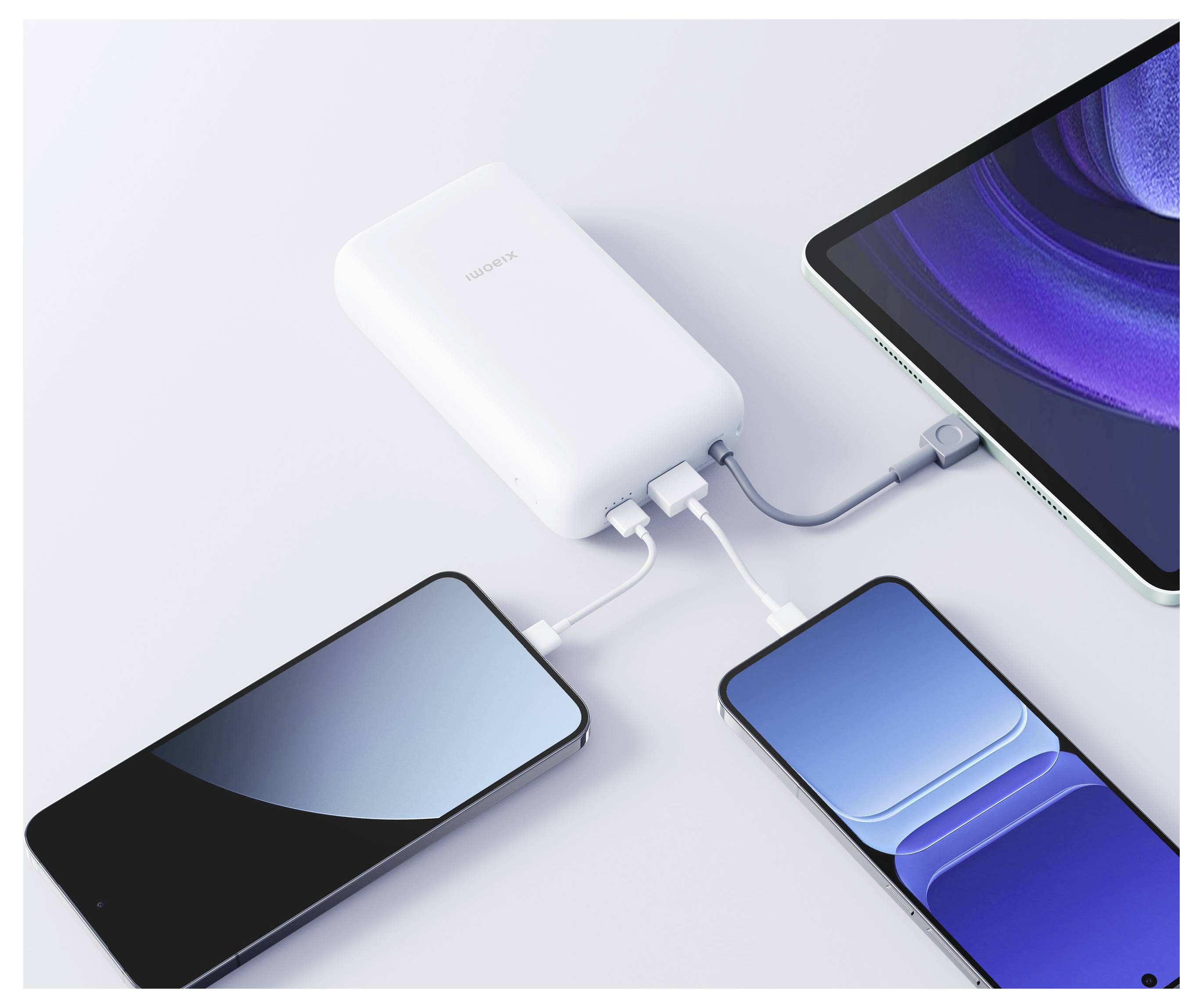 Bílá Huawei powerbanka nabíjí tři zařízení: telefon, tablet a další telefon připojené kabely na světlém povrchu.