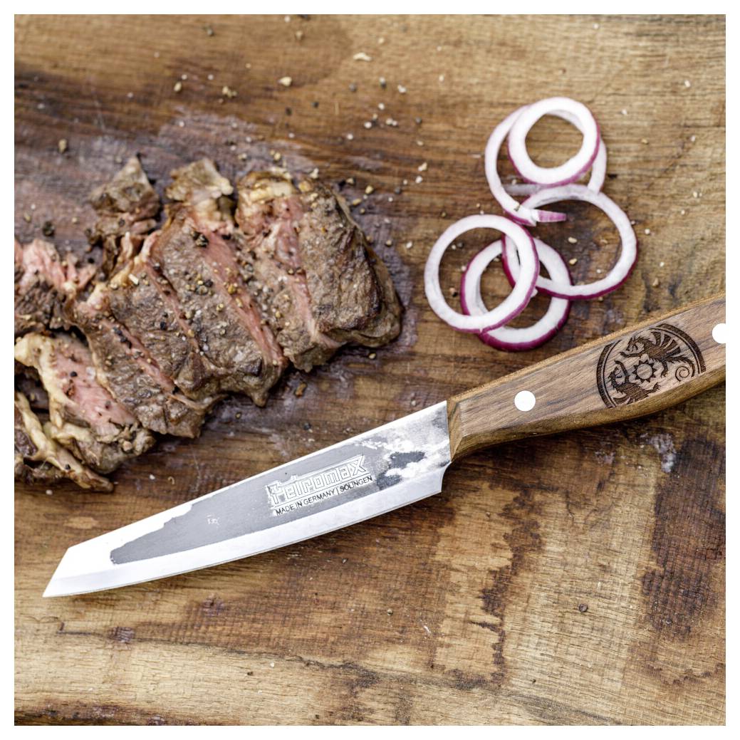 Nakrájený grilovaný steak na dřevěné krájecí desce s kroužky červené cibule a kuchyňský nůž na krájení s dřevěnou rukojetí