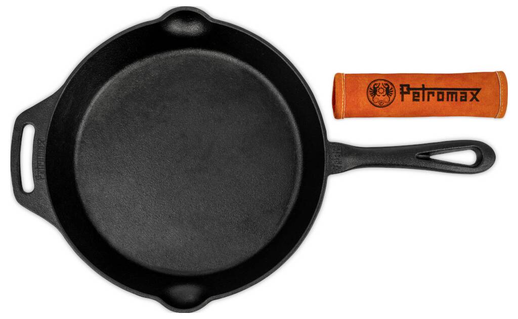 Černá litinová pánev se dvěma uchy vedle oranžového ochranného obalu na rukojeť značky "Petromax" na bílém pozadí.