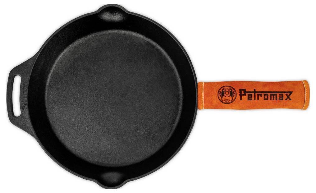 Černá litinová pánev s oranžovou rukojetí "Petromax" na bílém pozadí, pohled shora.