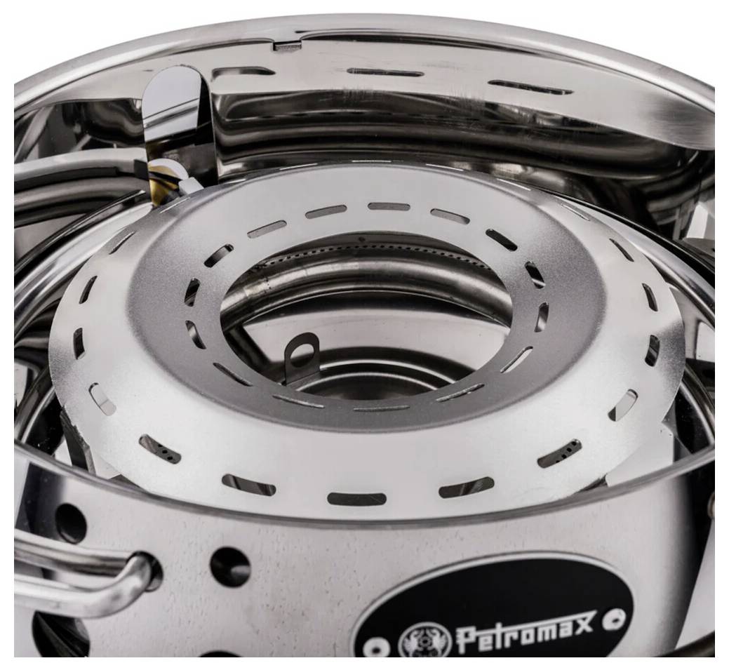 Detailní záběr hořáku nerezového kempovacího vařiče s ventilačními otvory a značkou "Petromax" na těle.