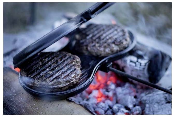 Dva hamburgery grilované v litinové pánvi na rozpálených uhlících