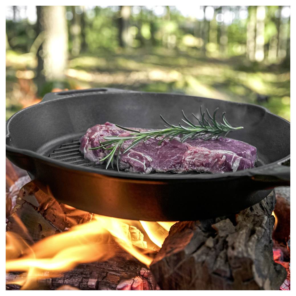 Surové maso se rozmarýnem se připraví na rozpálené litinové pánvi nad otevřeným kcampákovým ohněm v lesnatém venkovním prostředí.