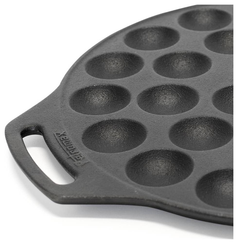 Detailní pohled na kulatou litinovou pánev na takoyaki s množstvím mělkých jamek a bočním madlem.