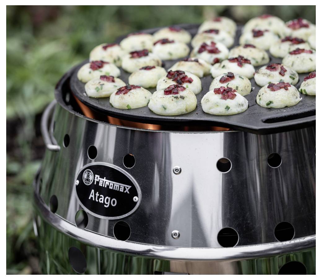 Venkovní gril s kulatou pánví péči malých knedlíčků nebo plněných kousků vrchovatých bylinkami a červeným kořením na kamnech Petromax Atago.