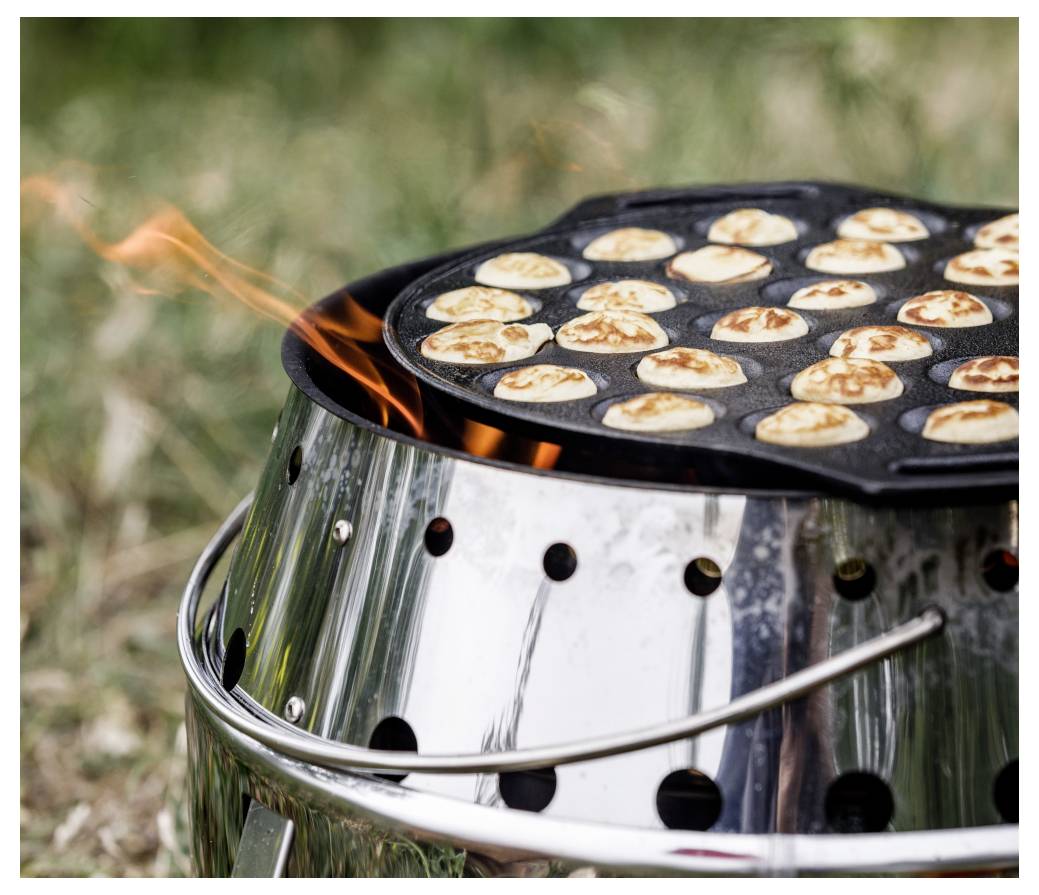 Malé lívance vaří se na kulaté plotně nad venkovním grillem na dřevěné uhlí s viditelnými plamenům.