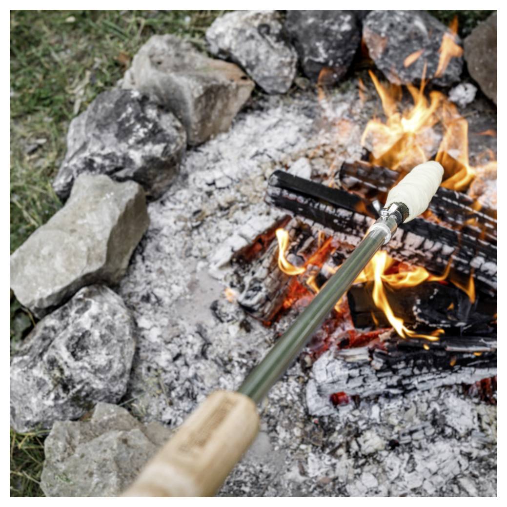 Marshmallow na páce na opékání drženou nad koulí s ohněm obklopenou kameny a hořícími kusy dřeva.