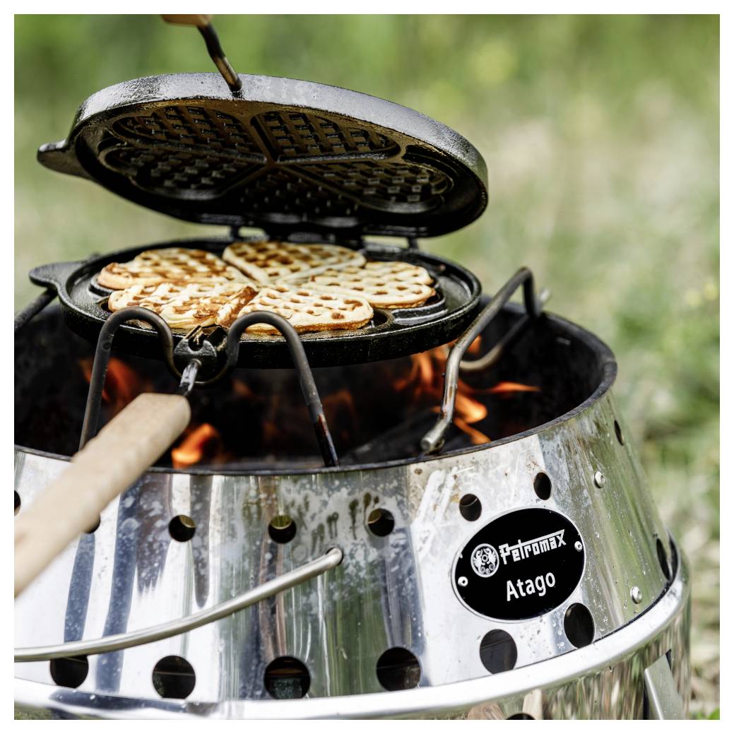 Vaflovač vaří vafle nad otevřeným ohněm na přenosném venkovním grilu.