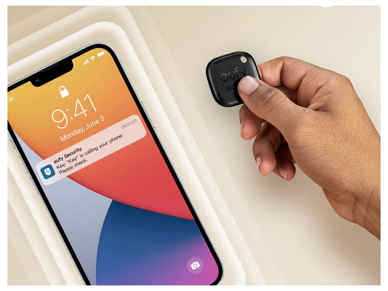Ruka drží černý sledovač klíčů „eufy Security" vedle smartphonu, který zobrazuje zámkovou obrazovku a upozornění „Klíč se blíží k telefonu".