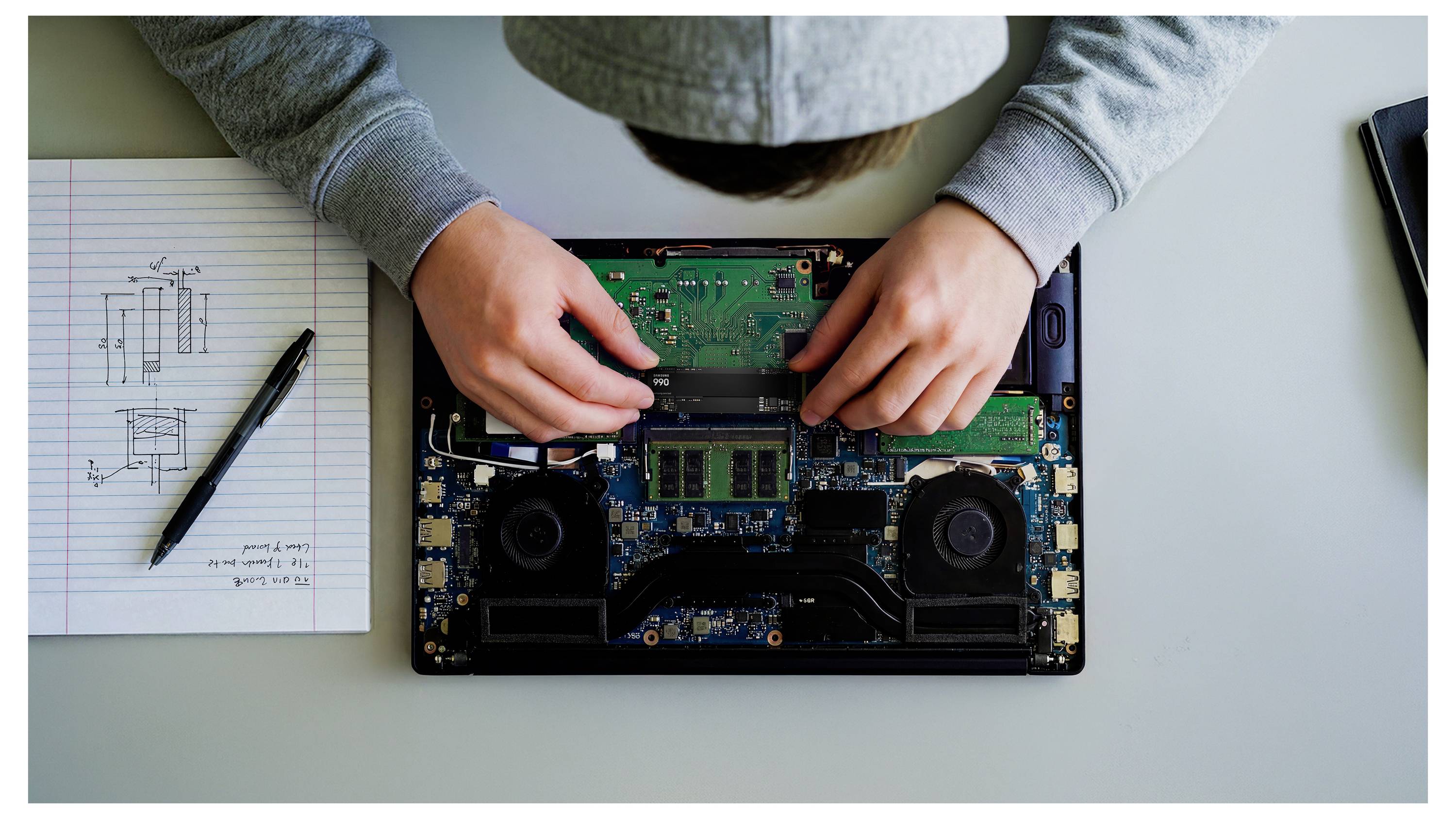 Ruční oprava laptopu na ploše stolu, s nástroji a poznámkami k obvodům vedle něj.
