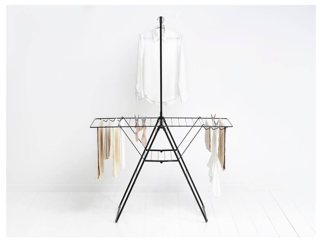 Minimalistický stojan na oblečení s bílou halenkou umístěnou uprostřed nad visícími šálami nebo pásy na obou stranách v jasné, prázdné místnosti.