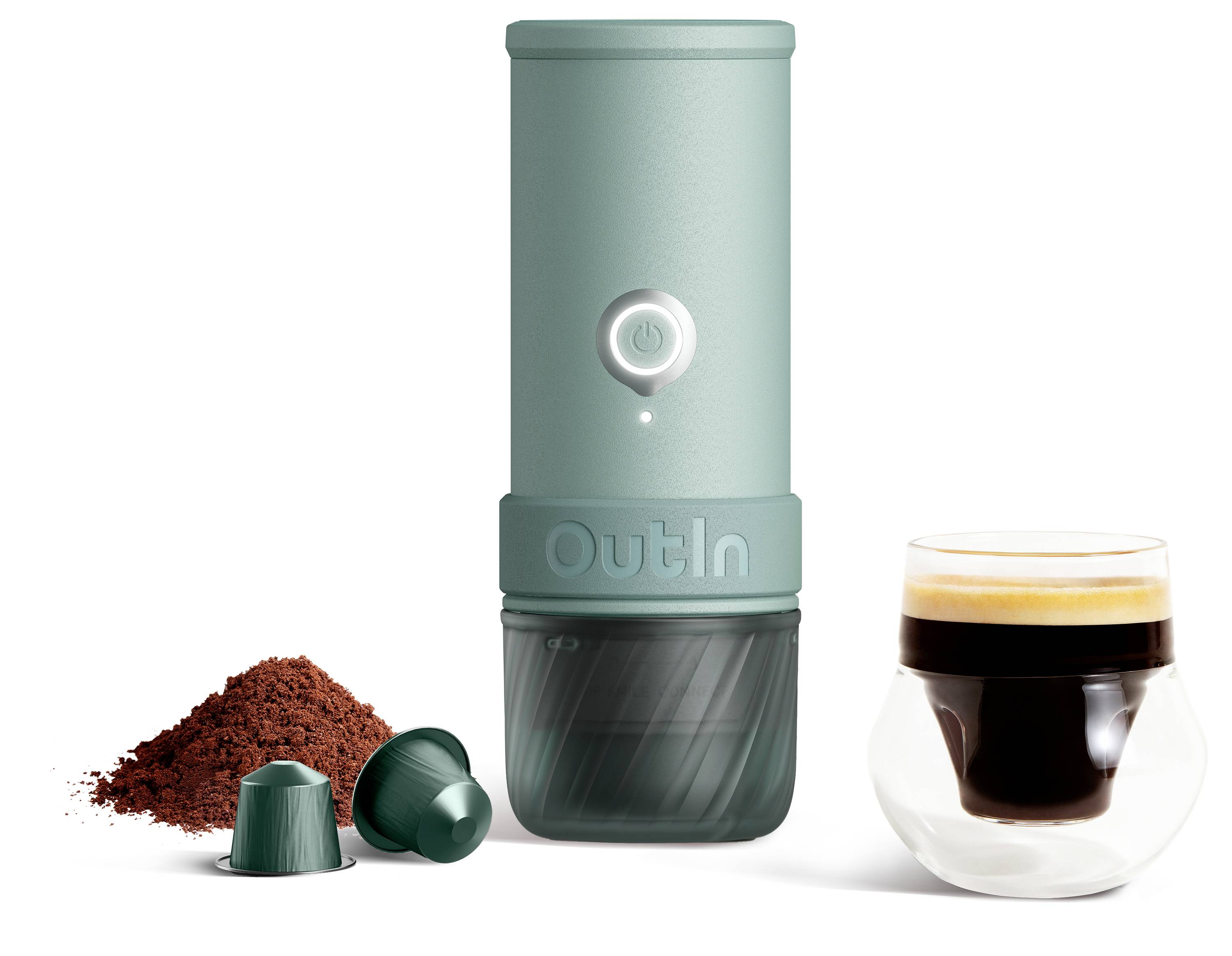Přenosný kávovar v barvě máty s tlačítkem napájení, zobrazený vedle kávového prášku, dvou kapsulí a sklenice s espresso nápoji.