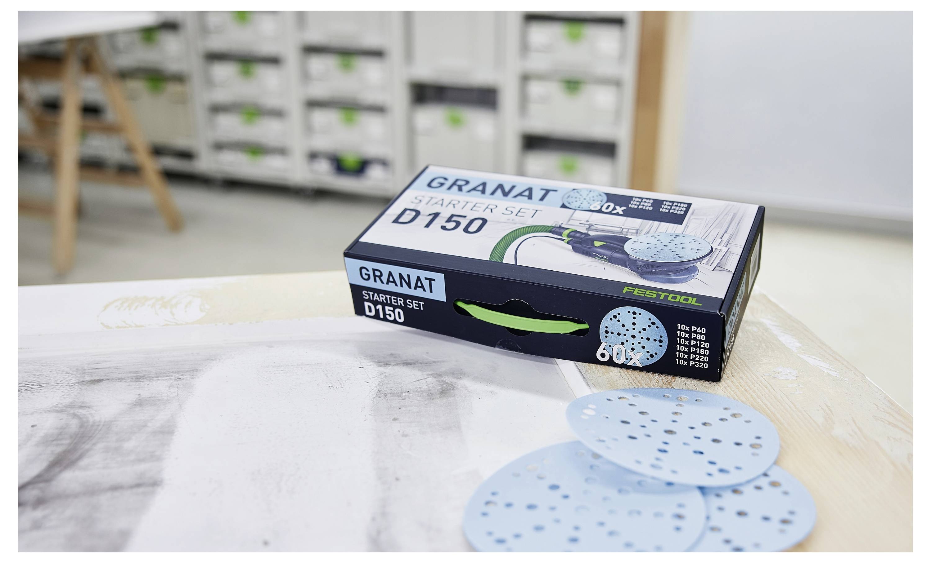 Festool GRANAT Startovací sada D150 na pracovním stole s modrými brousnými disky rozloženými vedle ní v dílně.