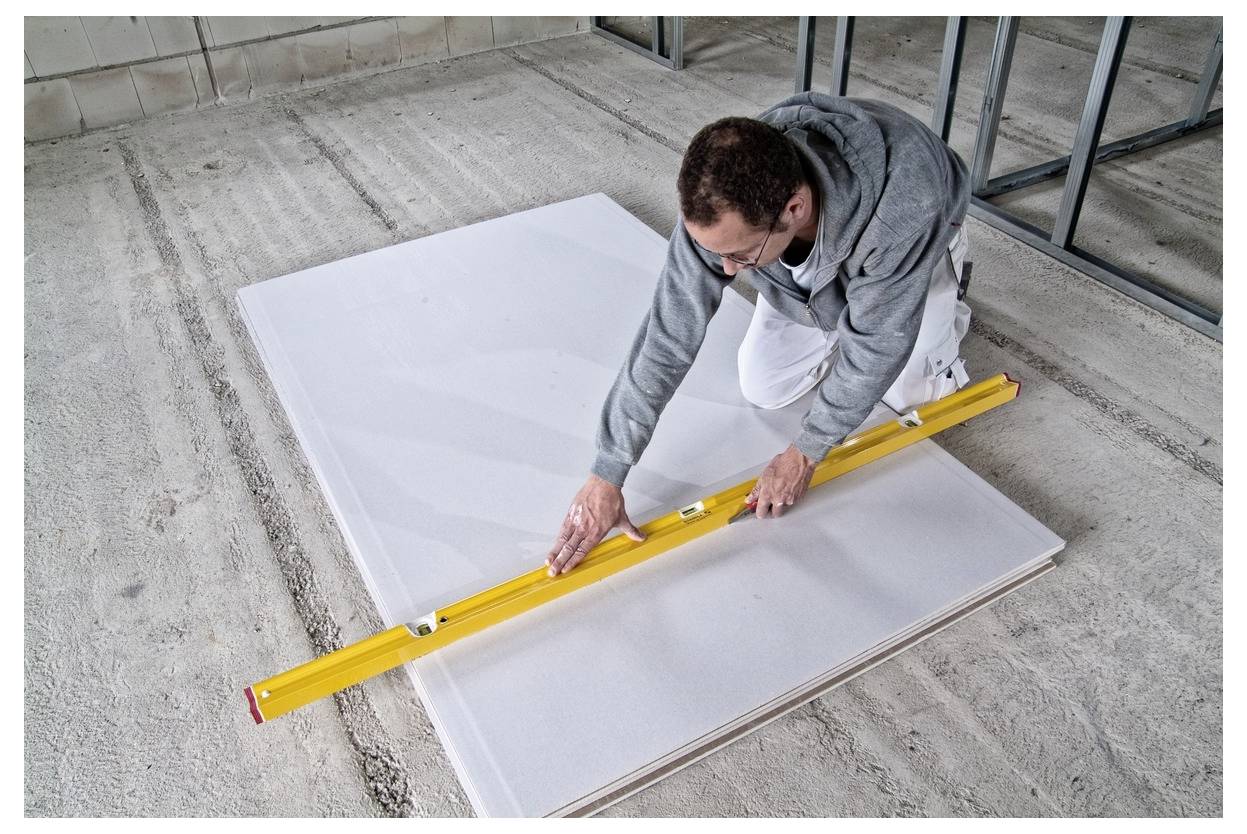 Pracovník měřící velký bílý panel žlutou vodováhou na betonové podlaze v construcci stavební oblasti.