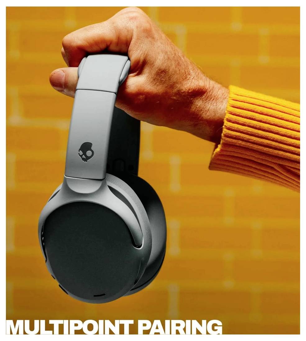 Ruka držící šedá uzavřená sluchátka Skullcandy na oranžovém pozadí s textem 'MULTIPOINT PAIRING' v dolní části.