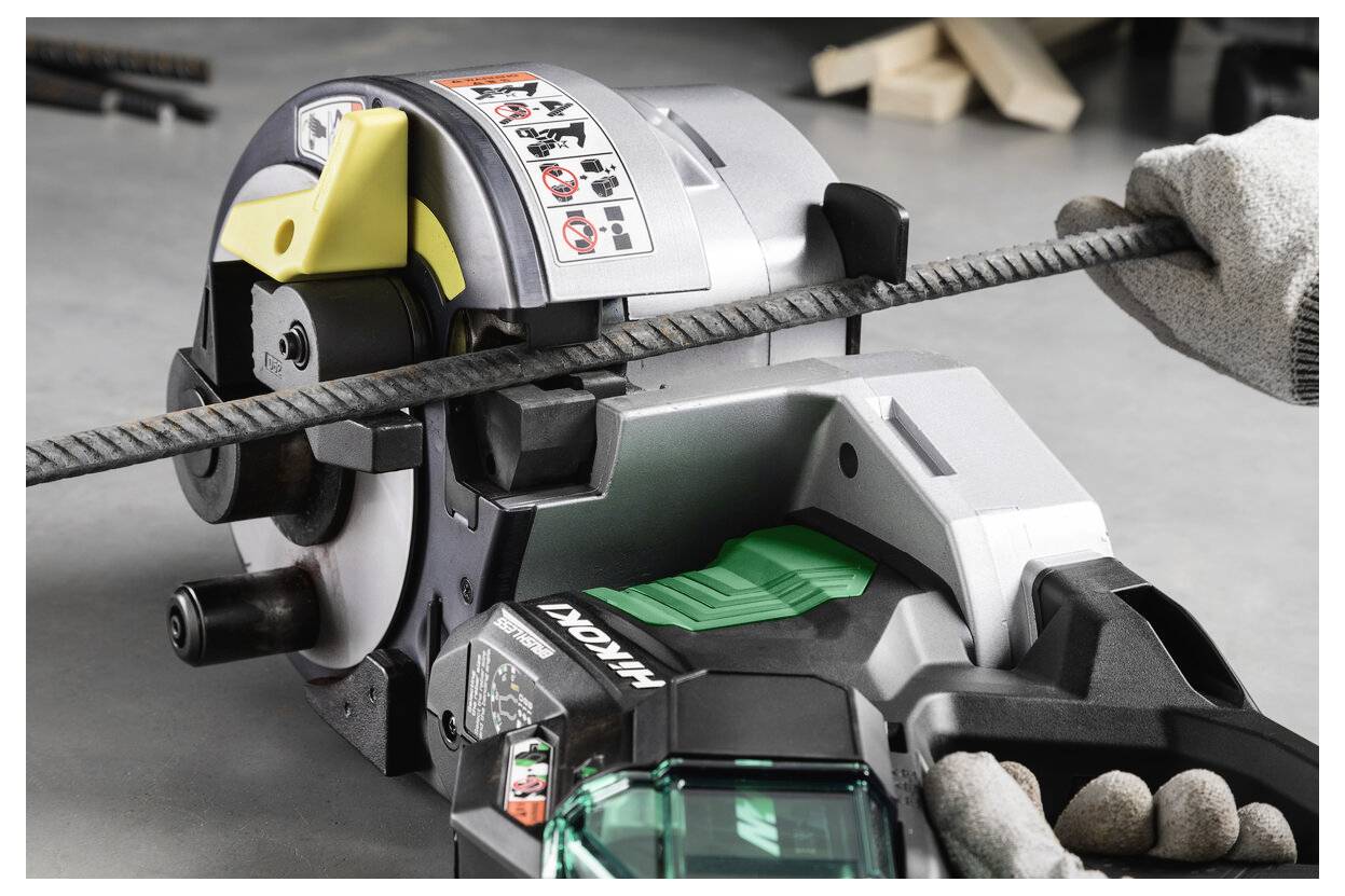 Osoba používá řezačku výztuže Makita k řezání ocelové tyče v rukavicích držící nástroj a tyč na podlaze dílny.