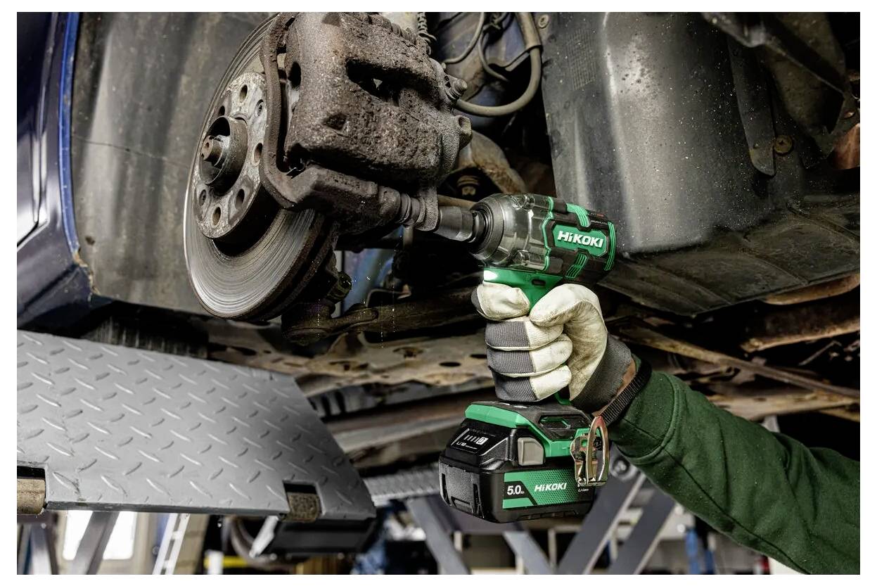 Mechanik používá bezšňůrový ráčnický příklepový nářadí k odejmutí šroubu kola automobilu, zatímco je vozidlo zvednuté na servisní platformě.