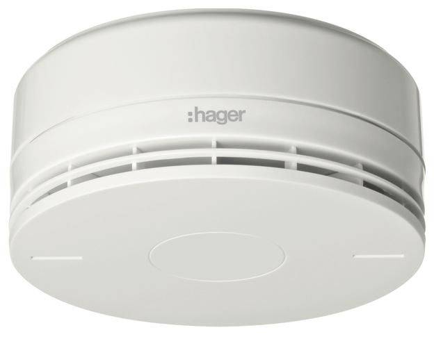 Bílý detektor kouře Hager s kruhovými ventilačními otvory a centrálním testovacím tlačítkem, zobrazený na jednobarevném pozadí.