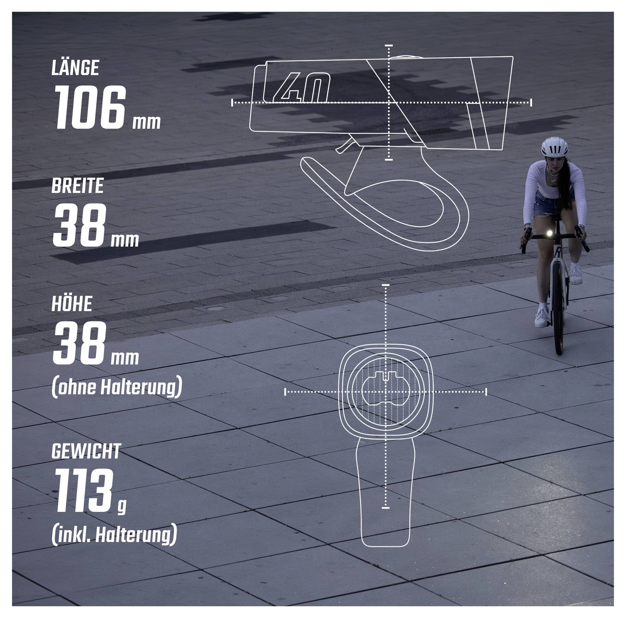 Graf se rozměry produktu součásti kola: délka 106 mm, šířka 38 mm, výška 38 mm bez držáku, hmotnost 113 g včetně držáku; cyklista v pozadí.