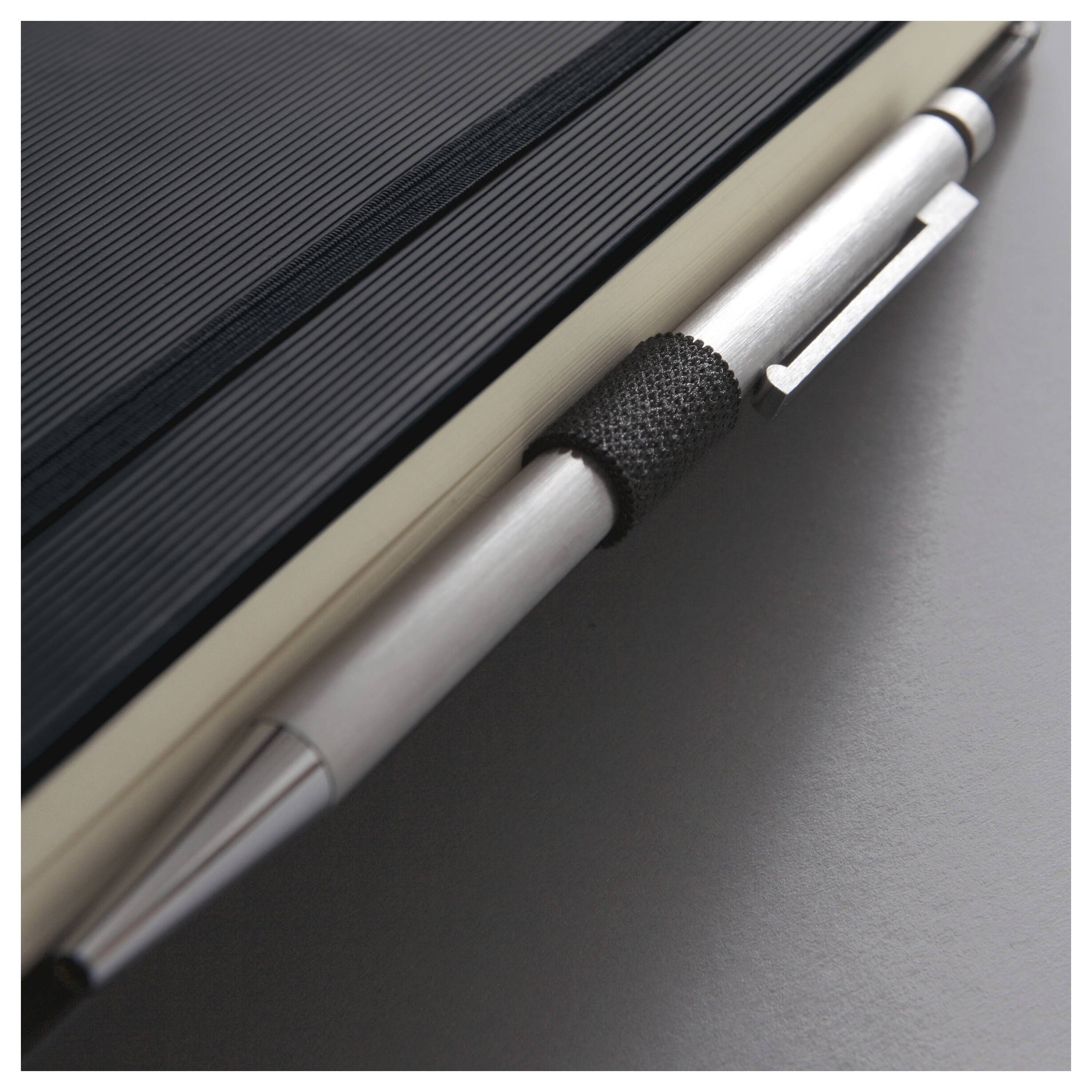 Detailní snímek stříbrného pera upevněného na černém spirálovém notebooku na tmavém povrchu.