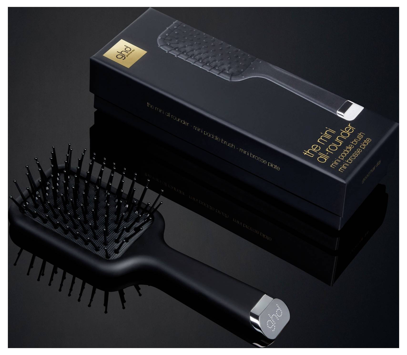 Černý hřeben na vlasy s kovovými hroty vláken zobrazený vedle své krabicové balení, označený „the mini detangler" se zlatým textem.