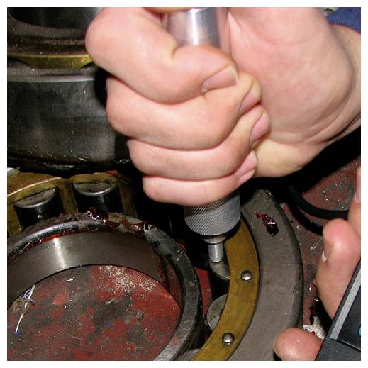 Detailní záběr rukou používajících ruční nástroj k utažení nebo nastavení součástky uvnitř mechanického zařízení.