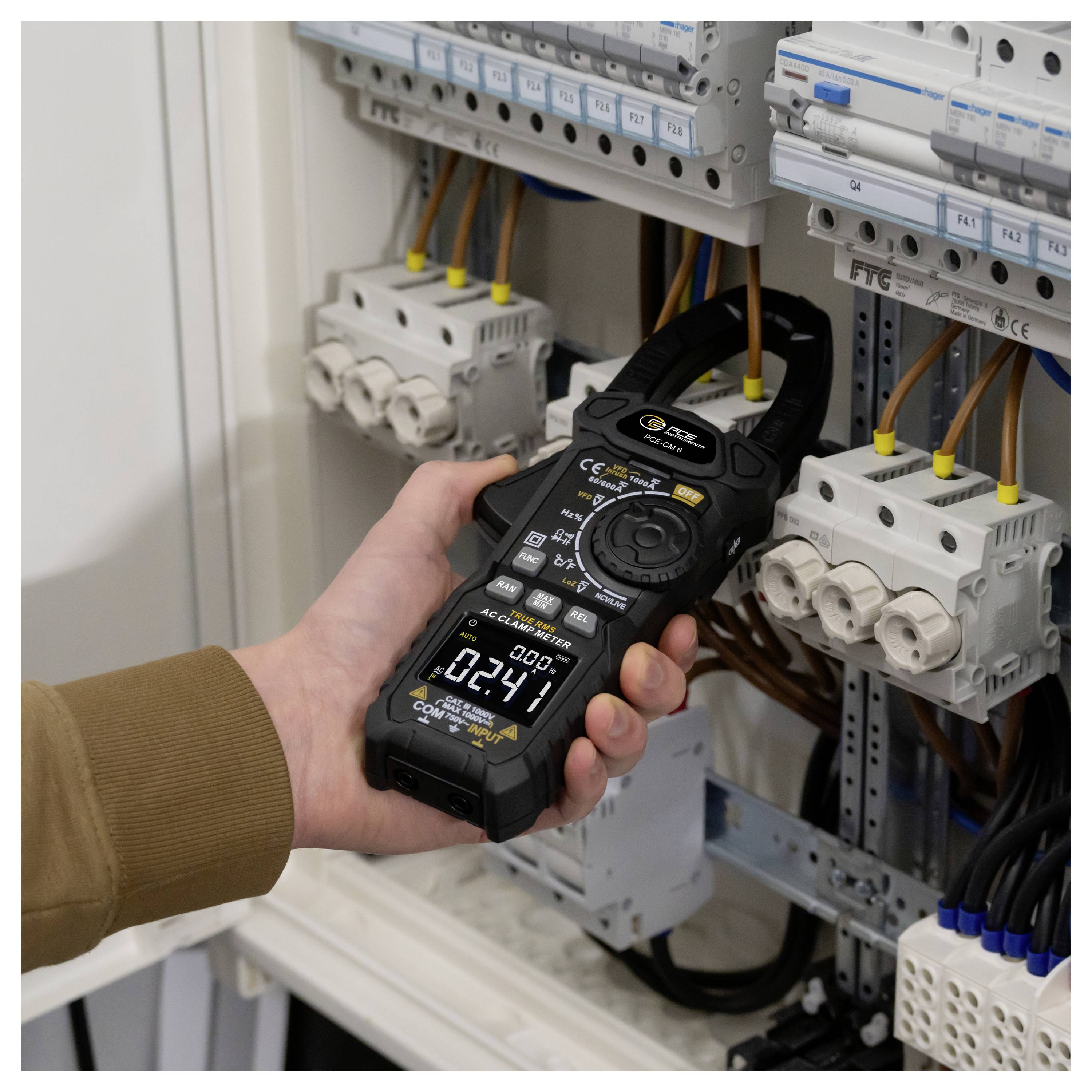 Ruční elektrikářský kleštový ampérmetr testující vedení uvnitř otevřeného elektrického ovládacího panelu s jističi a připojenými kabely.