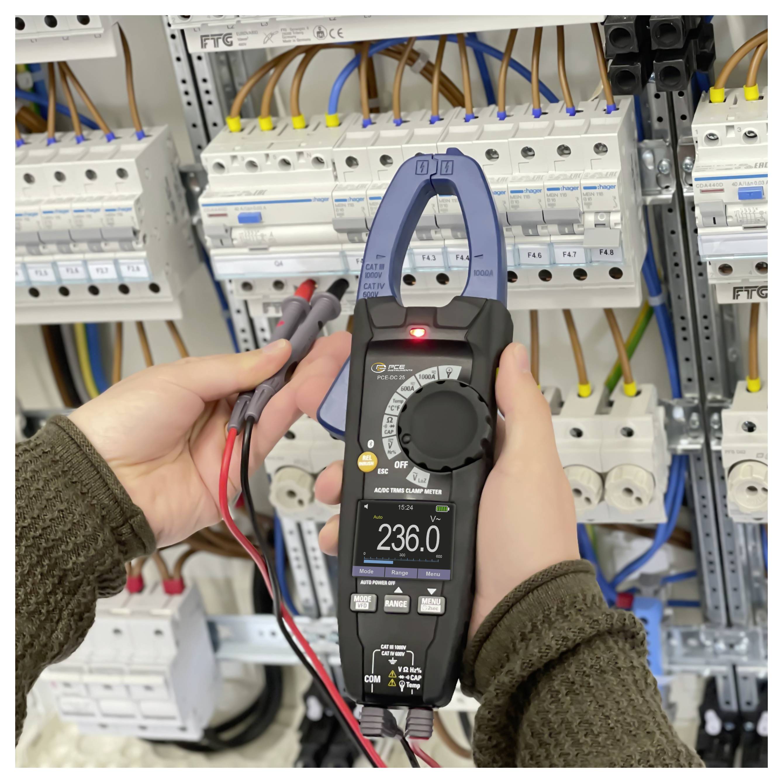 Osoba testující elektrický panel pomocí digitálního ampérmetru s kleštěmi, který ukazuje 236,0 voltů, obklopená jističi a elektrickým vedením.