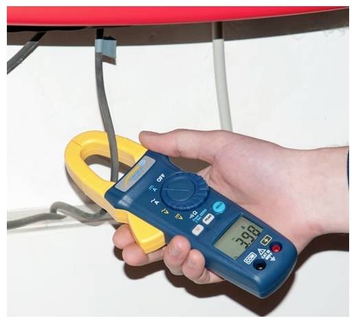 Ruka používající digitální multimetr se svorkou k měření elektrického kabelu s digitálním displejem ukazujícím přibližně 39,8.