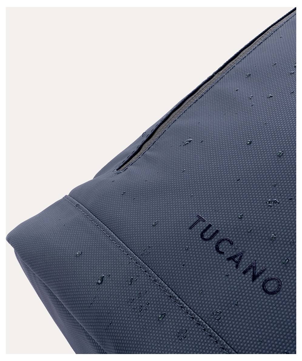 Detailní snímek rohu tmavě modné tašky nebo batohu Tucano s kapkami vody na povrchu před světlým pozadím.