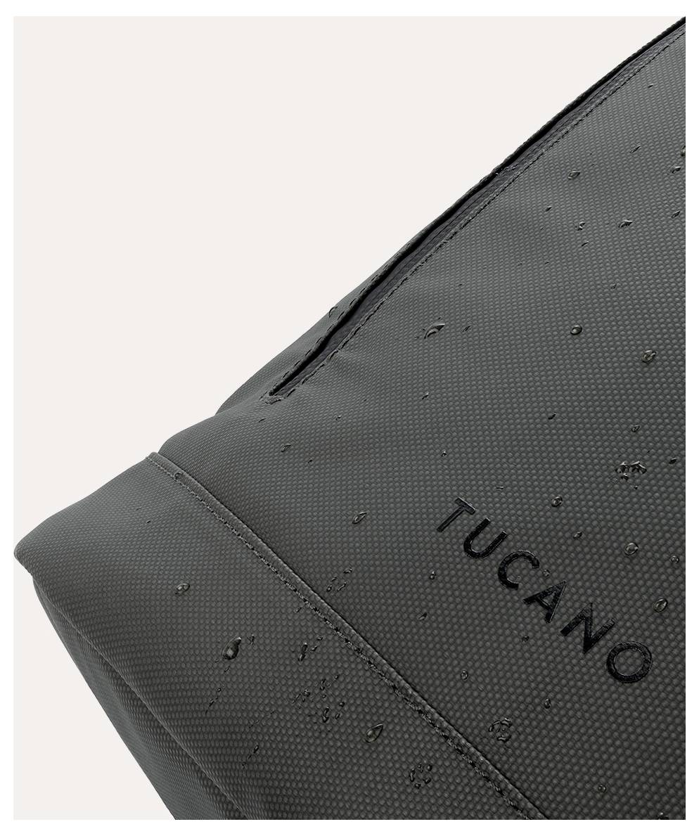 Detailní snímek černé voděodolné tašky nebo pouzdra Tucano s viditelnými kapkami deště na strukturovaném povrchu.