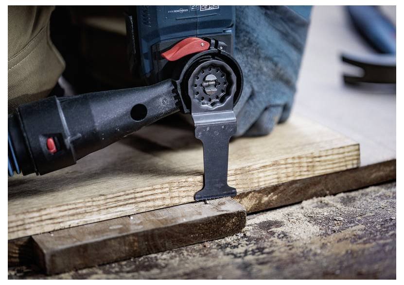 Detailní záběr na elektrickém nářadí řezajícím do dřevěné desky na pracovní lavici, s rozptýleným pilním prachem v okolí.