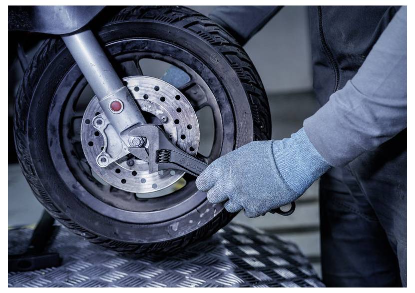 Mechanik v rukavicích používá klíč k nastavení brzdového systému přední koly motocyklu v dílně.