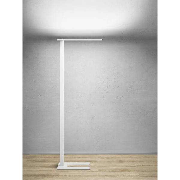 Minimalistická bílá stojací lampa stojící na dřevěné podlaze u šedé zdi, se štíhlým svislým stojanem a horní lištou pod reflektorem.