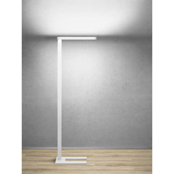 Minimalistická bílá stojací lampa s horním osvětlením nad prázdnou šedou stěnou a dřevěnou podlahou.