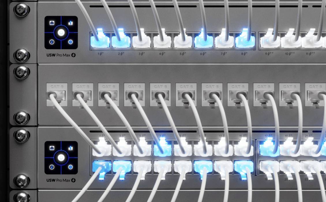Síťový přepínač s mnoha připojenými ethernetovými kabely, několik portů svítí modře, což indikuje aktivní spoje.