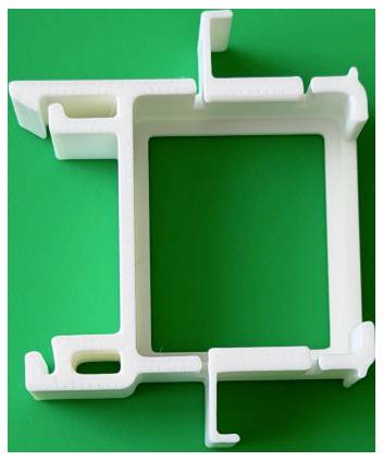 Bílý plastový rám nebo držák s výřezy, zobrazený na jasně zeleném pozadí.