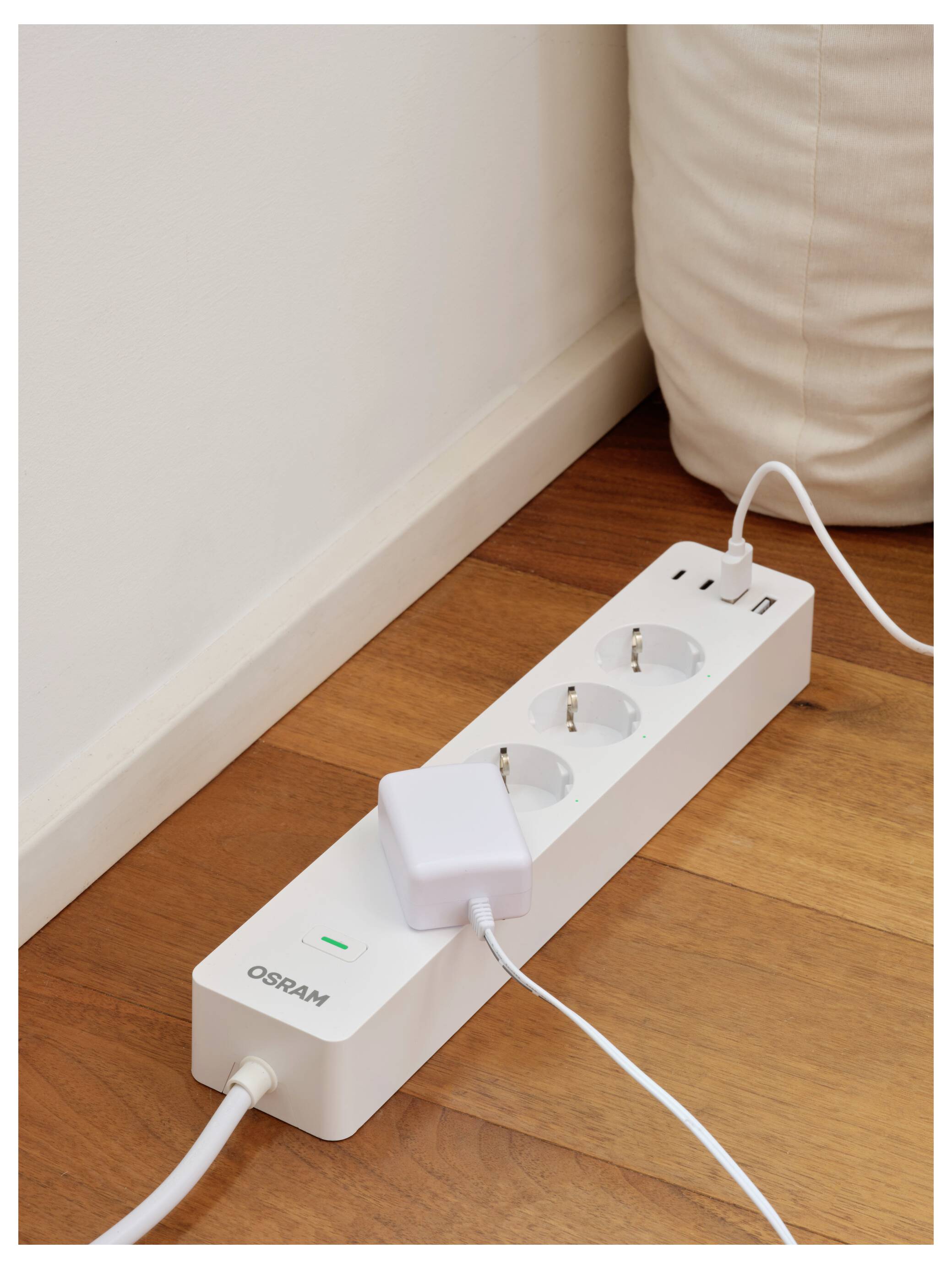 OSRAM prodlužovací kabel na dřevěné podlaze s připojenou nabíječkou, jednou obsazením zásuvkou a zeleným indikačním světlem.