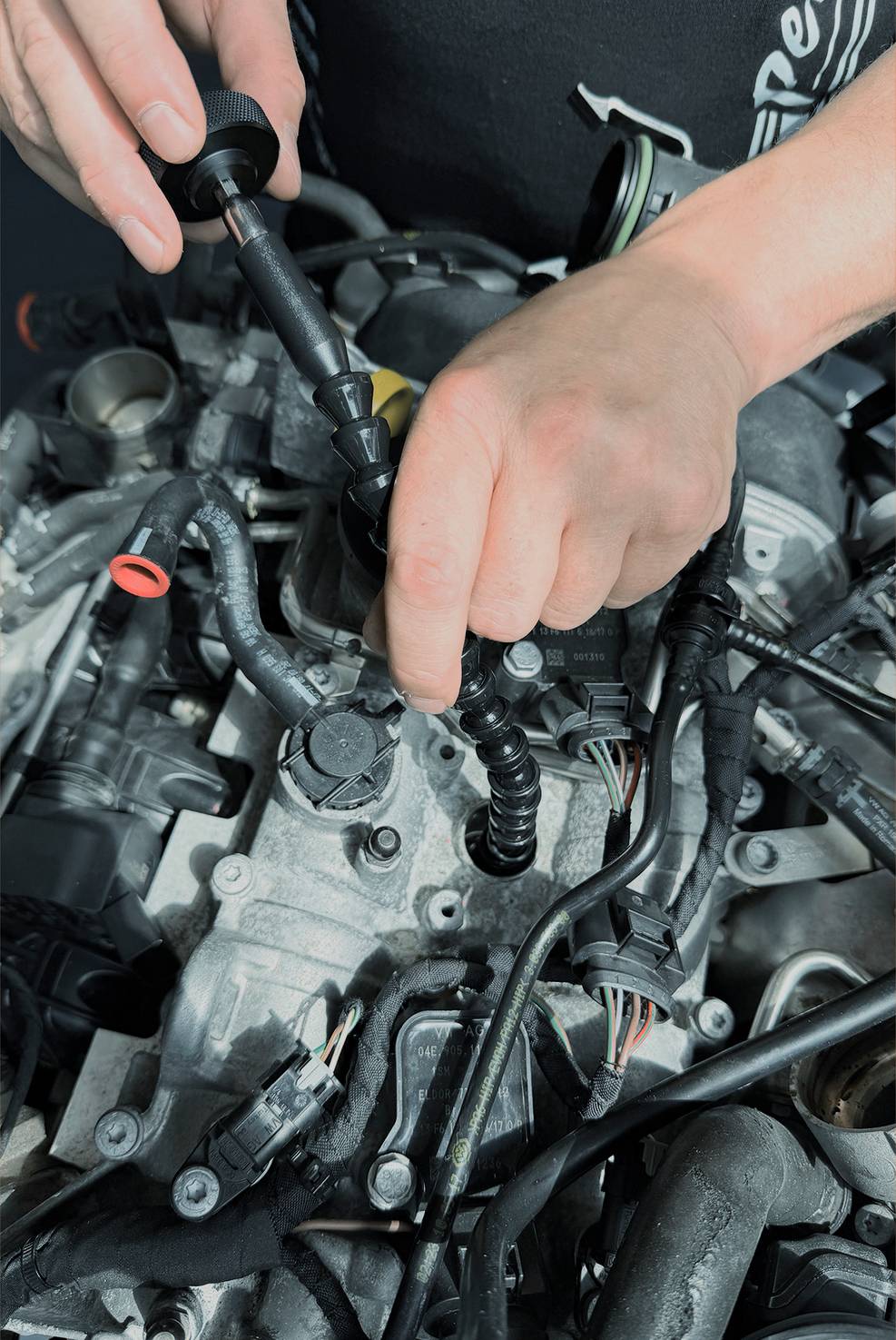 Ruce používající nástroj k opravě nebo kontrole složitého motoru s vyloupnutými hadičkami, vodiči a kovovými součástkami.