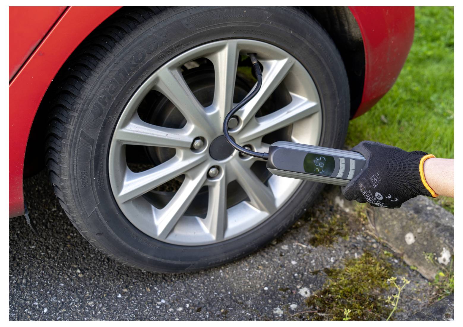 Rukavicí opatřená ruka používající digitální manometr na pneumatice automobilového kola ke kontrole tlaku vzduchu.