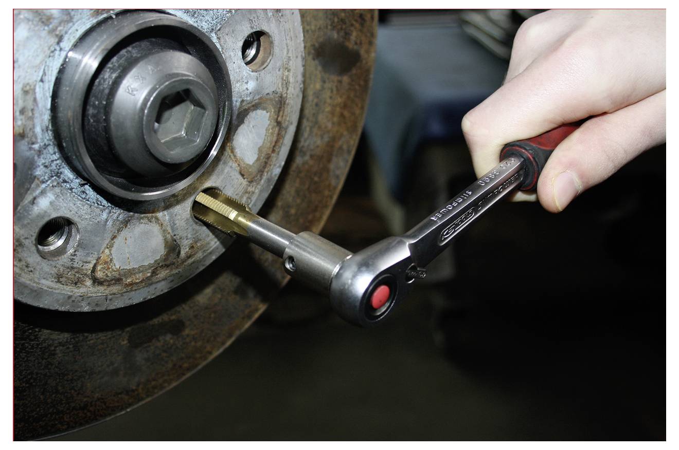 Detailní záběr na ruku používající račňový klíč k uvolnění šroubu na rezavém kovovém náboji kola nebo brzdovém mechanismu.