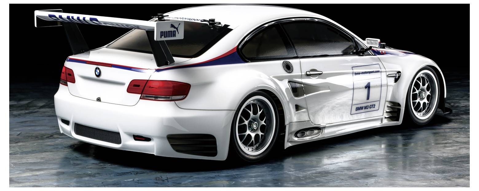Bílý závodní vůz BMW s číslem 1, velké zadní křídlo a závodní nálepky zobrazeny v bočním pohledu na studiové pozadí.