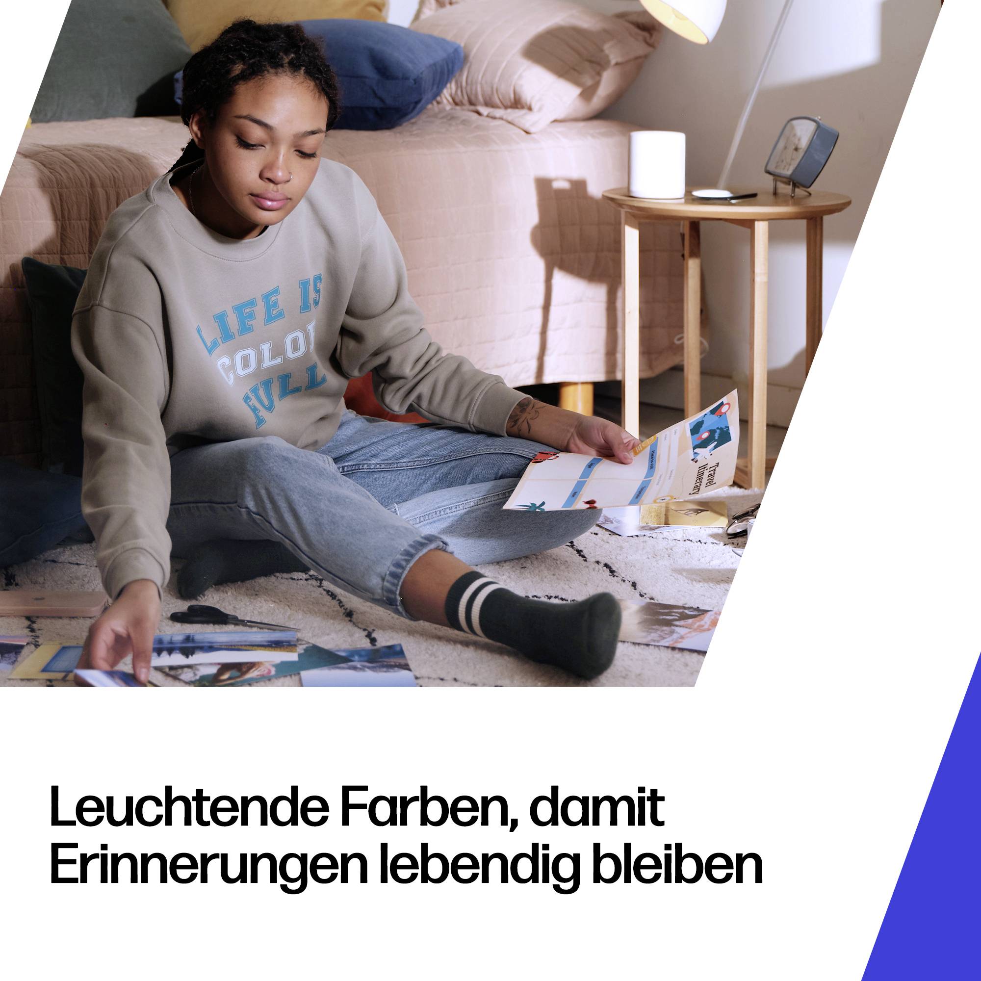 Žena sedící na podlaze v ložnici a prohlížející si vytištěné fotografie; německý text zní „Leuchtende Farben, damit Erinnerungen lebendig bleiben“ (živé barvy, aby vzpomínky zůstaly živé).