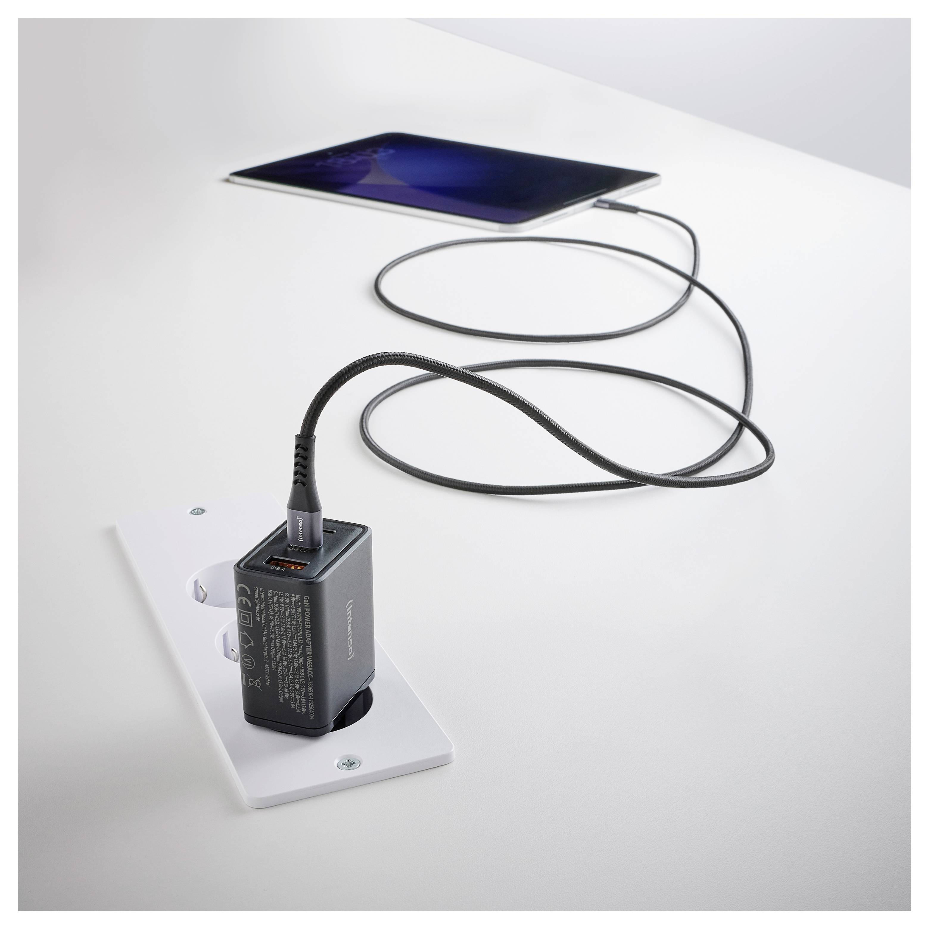 Tablet připojený kabelem na nástěnnou USB nabíječku, zobrazující drátové nabíjení.
