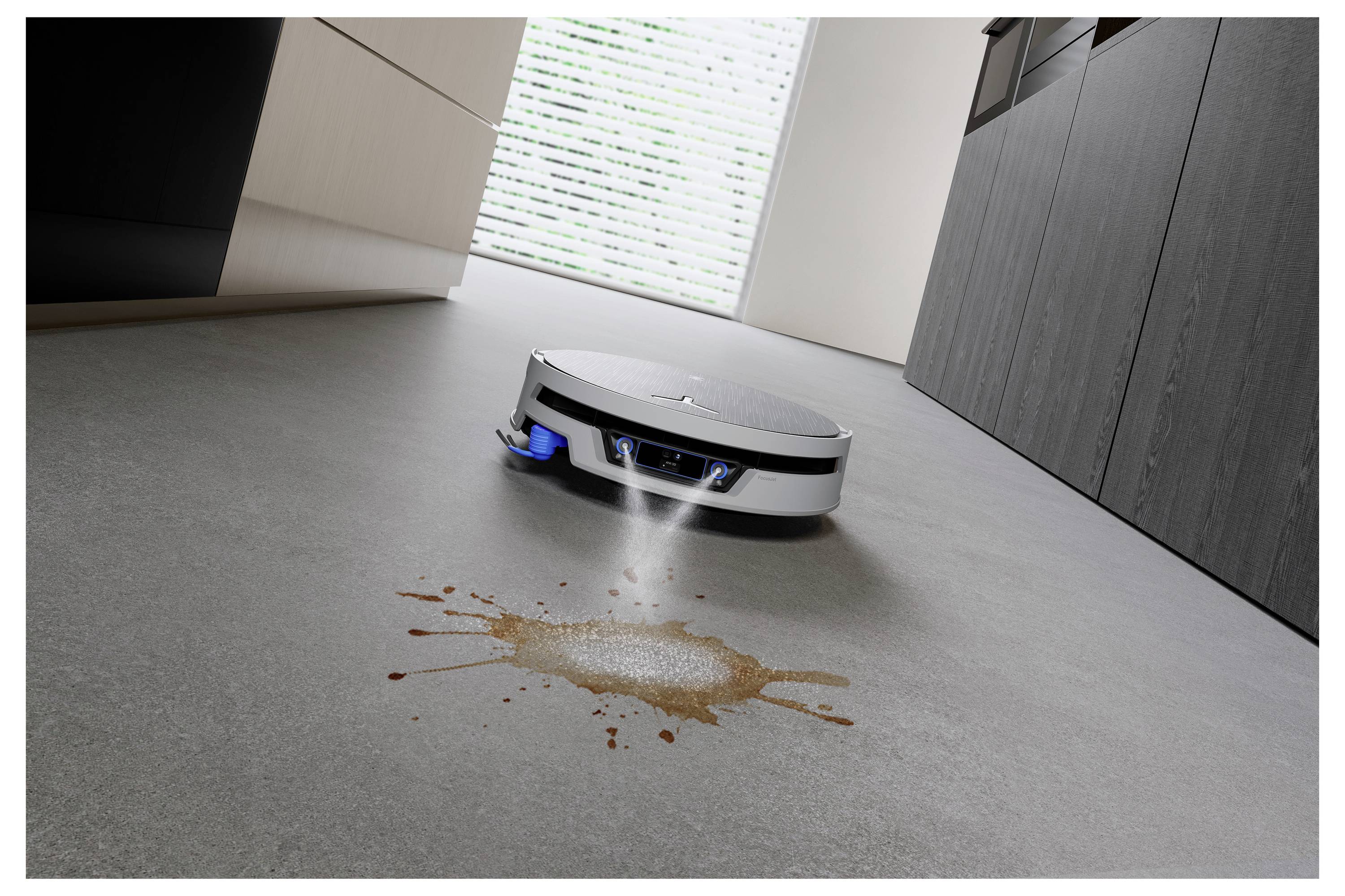 Robotický vysavač čistí rozlité kapaliny na kuchyňské podlaze, což demonstruje automatické čištění skvrn.