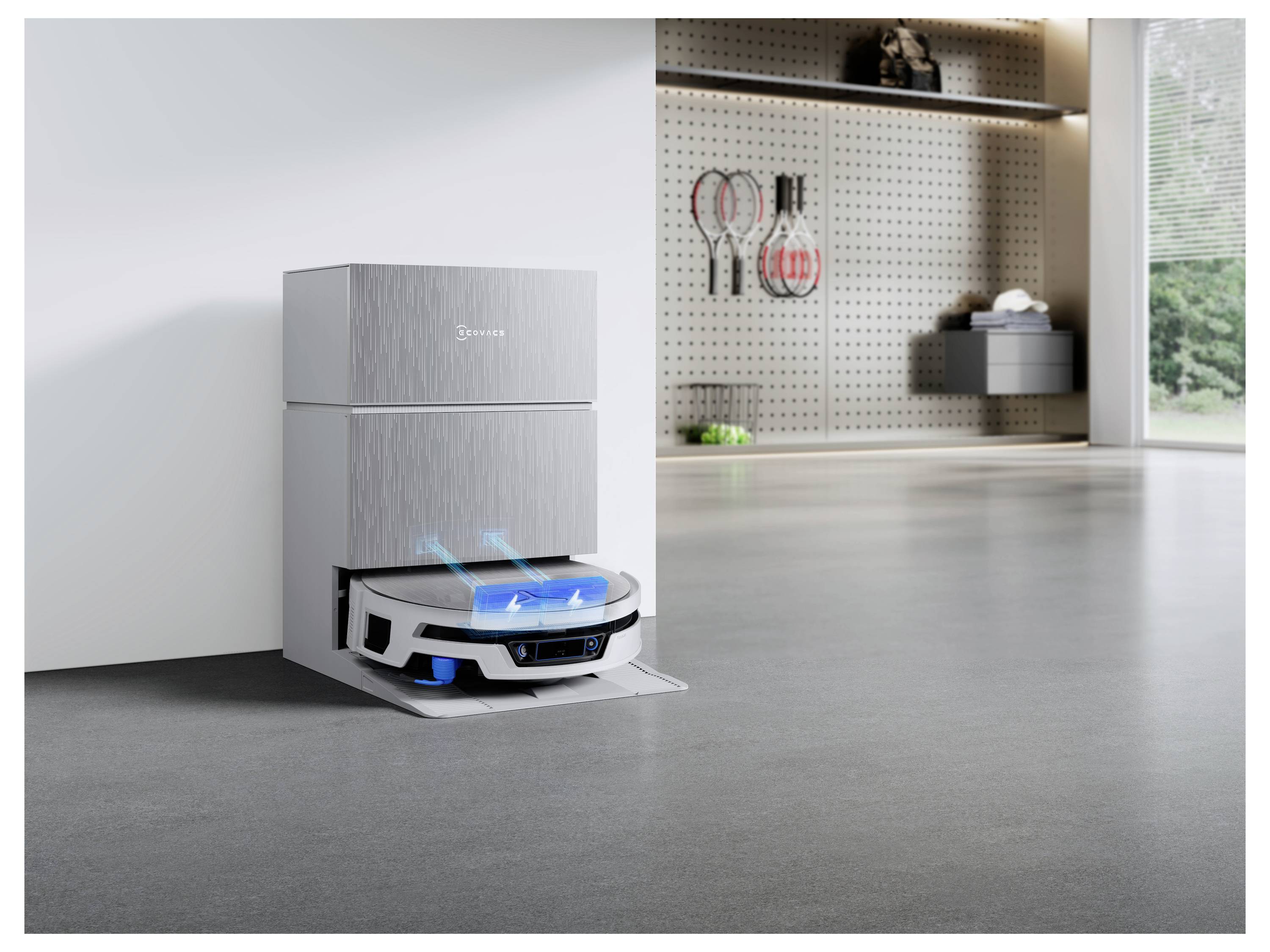 Robotický vysavač se parkuje a nabíjí vedle skříně v moderní místnosti s čistícími prostředky a jasným oknem v pozadí.