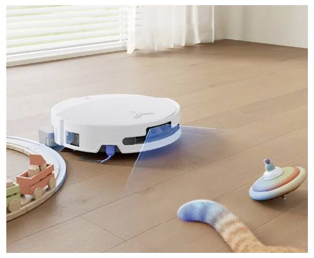 Bílý robotický vysavač čistí dřevěnou podlahu a současně vysílá modrý skenovací paprsek a vyhýbá se hračkám v jasně osvětlené místnosti.