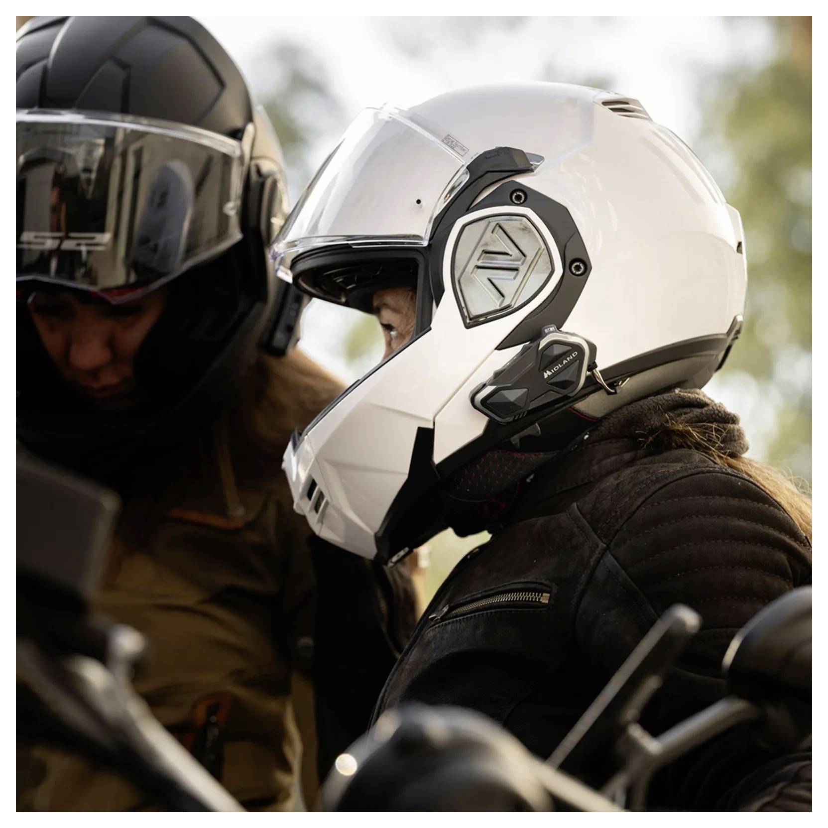 Dva motorkáři v přilbách, jeden v bílé a jeden v černé, sedí těsně vedle sebe na motorce venku.