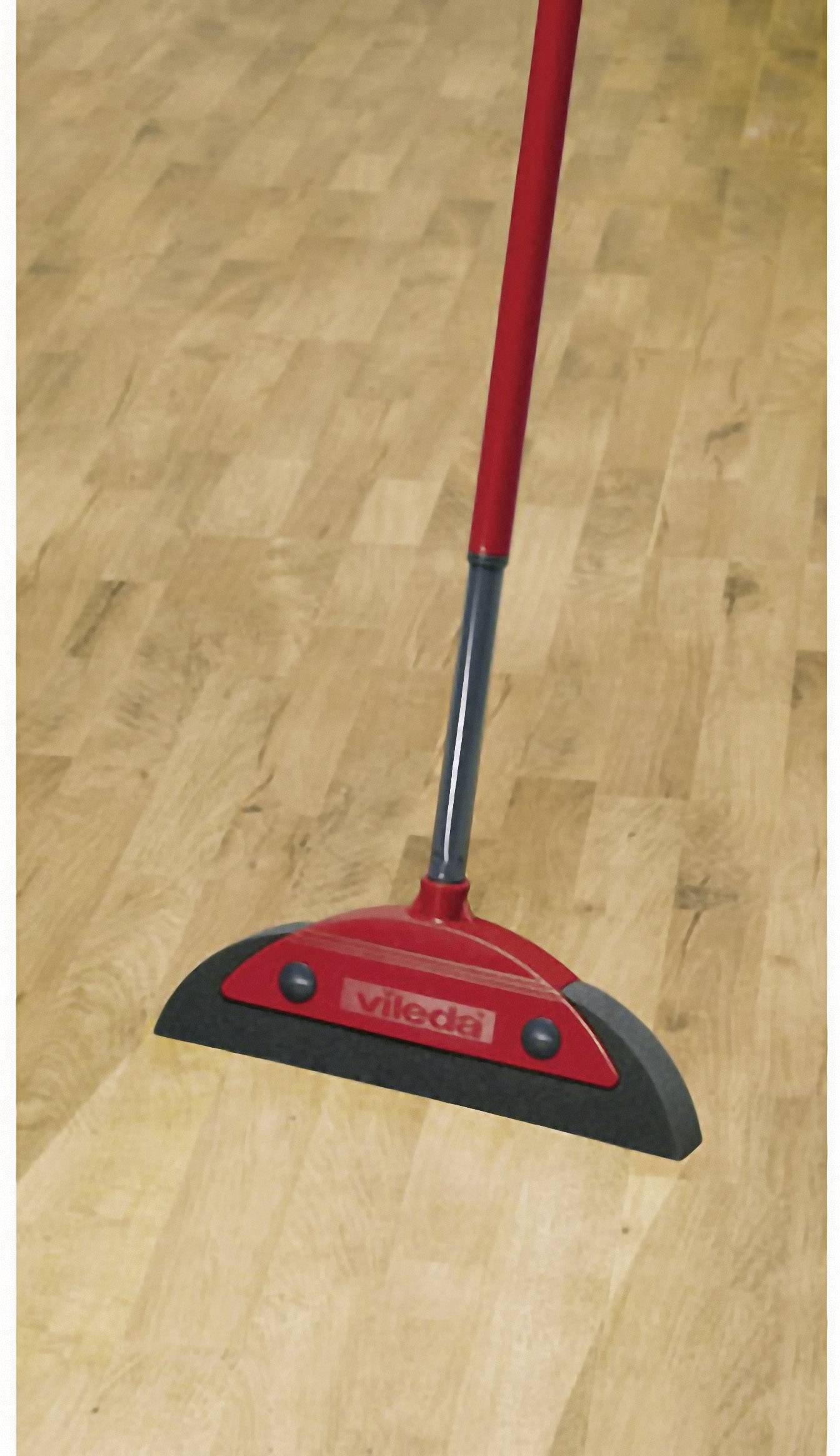 Smeták s červenou rukojetí a černou gumovou lištou stírá po dřevěné podlaze.