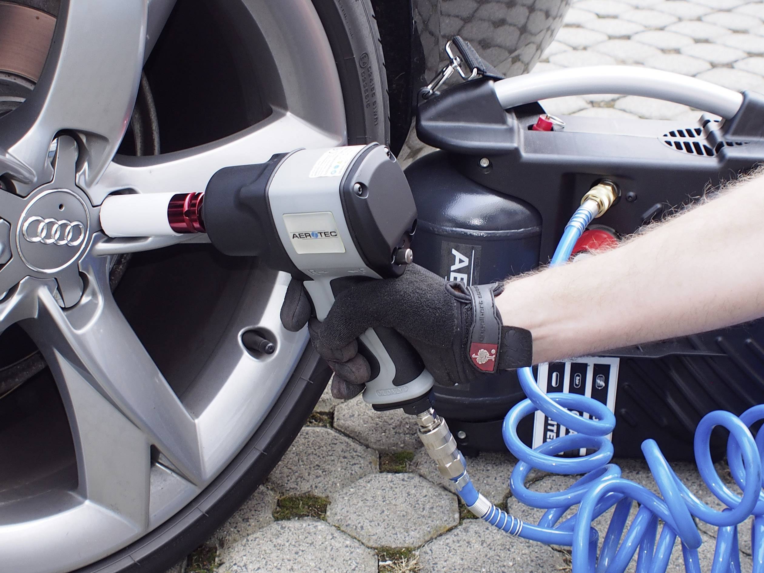 Osoba utahuje matici kola automobilu pomocí pneumatického utahováku.